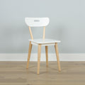 Minimalist white Scandinavian dining chair with light wood legs and handle-style cutout backrest against a pale gray wall