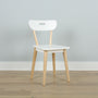 Minimalist white Scandinavian dining chair with light wood legs and handle-style cutout backrest against a pale gray wall