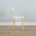 Minimalist Scandinavian wooden dining chair with white seat and backrest, natural wood legs on light hardwood floor against pale gray wall