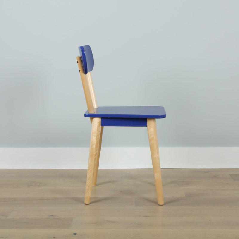 Minimalist blue wooden chair side profile with light wood legs on hardwood floor against a pale blue wall