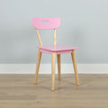 Pink children's chair with natural wooden legs on hardwood floor against pale gray wall