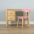 Light wood children's study desk with two drawers and pink wooden chair against pale gray wall