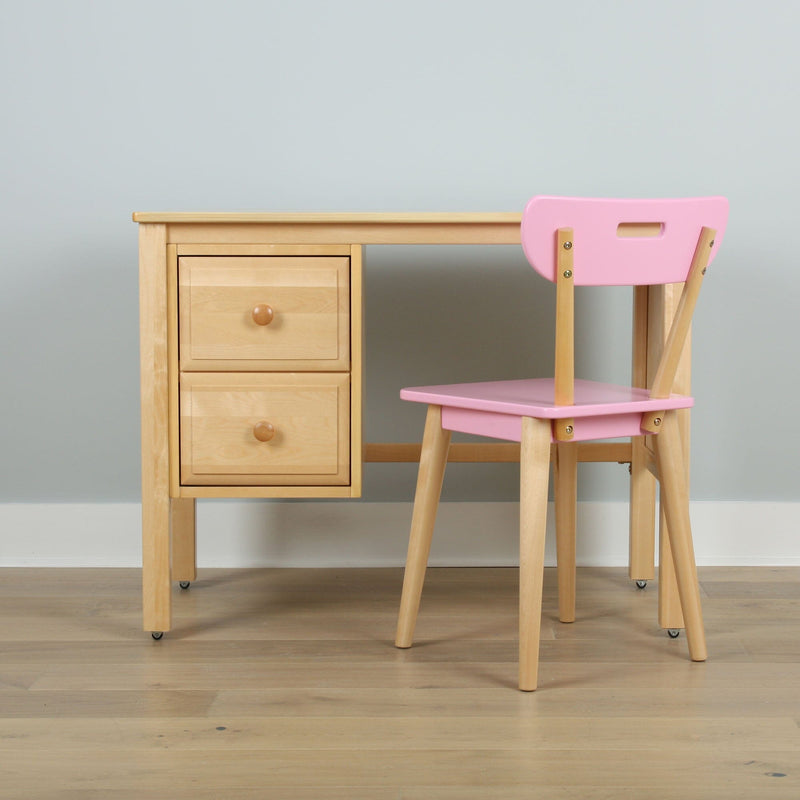 Light wood children's study desk with two drawers and pink wooden chair against pale gray wall