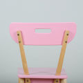 Close-up of a pastel pink wooden chair back with natural wood legs and rectangular handle cutout on a light gray background