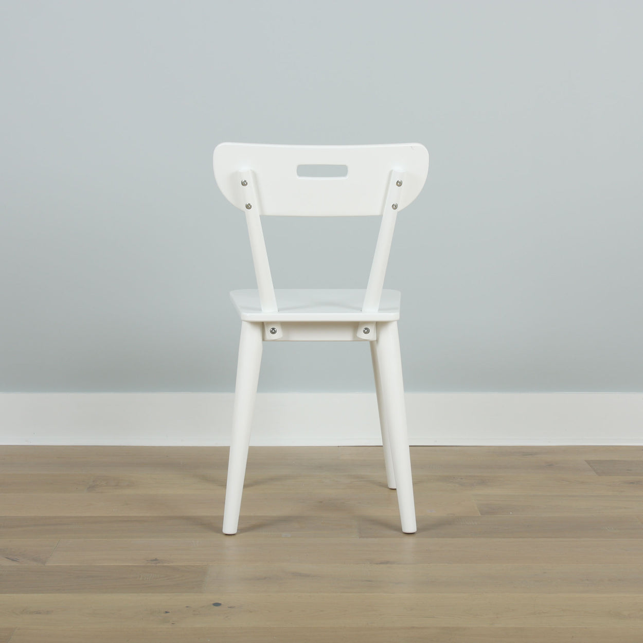 White wooden chair on a light wood floor against a pale gray wall.