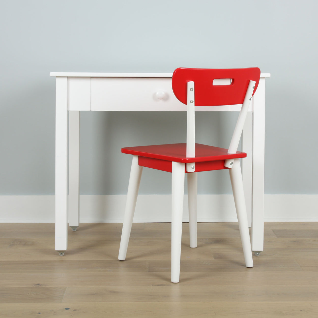 Child's red and white chair and desk set against light gray wall and wooden floor.