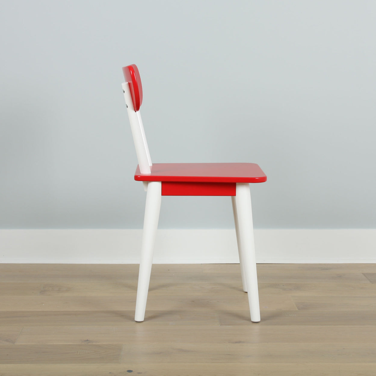 Red and white wooden chair with a modern design on a wooden floor against a light gray wall.