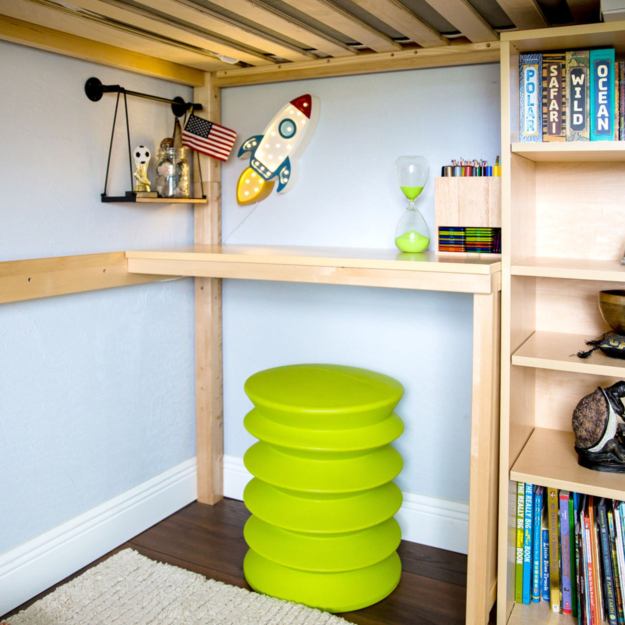 Child's room with green stool, rocket wall decor, hourglass, and bookshelves.