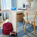 Home study desk for kids with white lamp and alarm clock, pencil cup and notebook, blue lunchbox, woven storage basket, white chair, red backpack and football on a blue rug