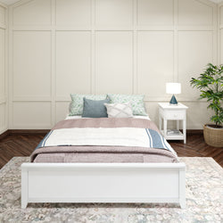 Elegant bedroom with a white wooden bed frame, cozy bedding, patterned pillows, a white bedside table with a lamp, and a potted plant for a serene ambiance.