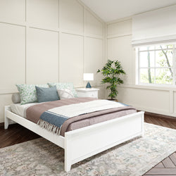 Modern bedroom interior with white bed and cozy pillows, featuring a bedside table and green plant by a window with natural light.