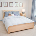 Kids bedroom with natural wood twin bed, blue gingham pillows, striped duvet, teddy bear and baseball, wooden nightstand with lamp, framed wall art