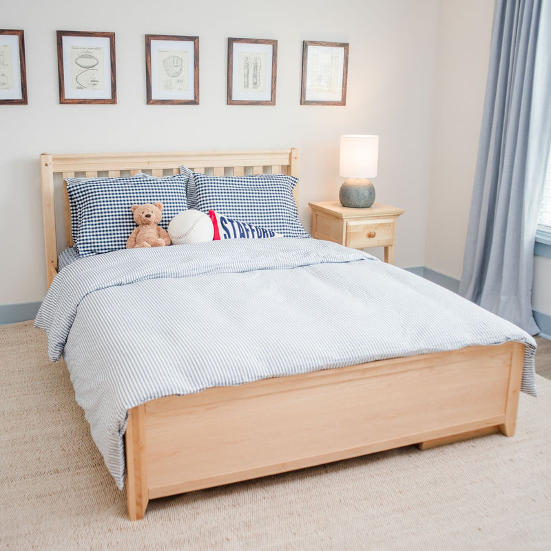 Kids bedroom with natural wood twin bed, blue gingham pillows, striped duvet, teddy bear and baseball, wooden nightstand with lamp, framed wall art