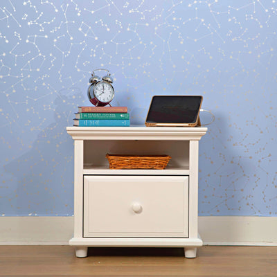 White nightstand with drawer, clock, books, tablet, and blue constellations wallpaper background.