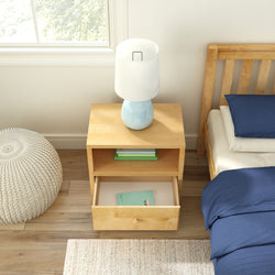 Wooden nightstand with blue lamp beside a bed with blue bedding.