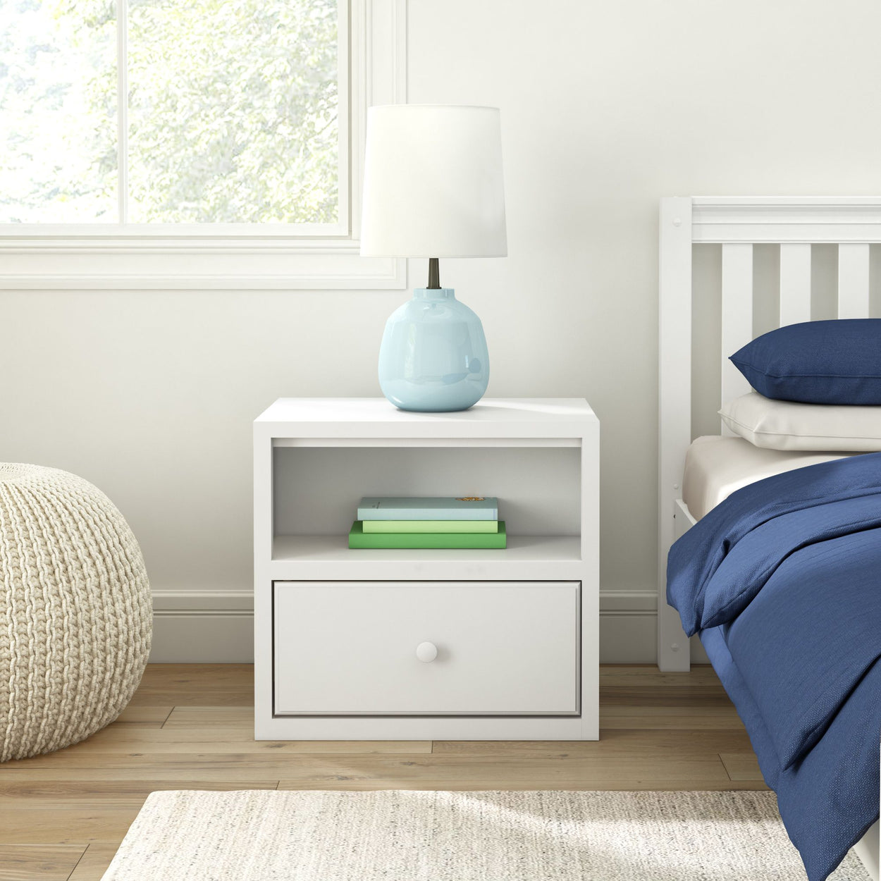 White bedside table with lamp, books, and navy bedding in modern bedroom.