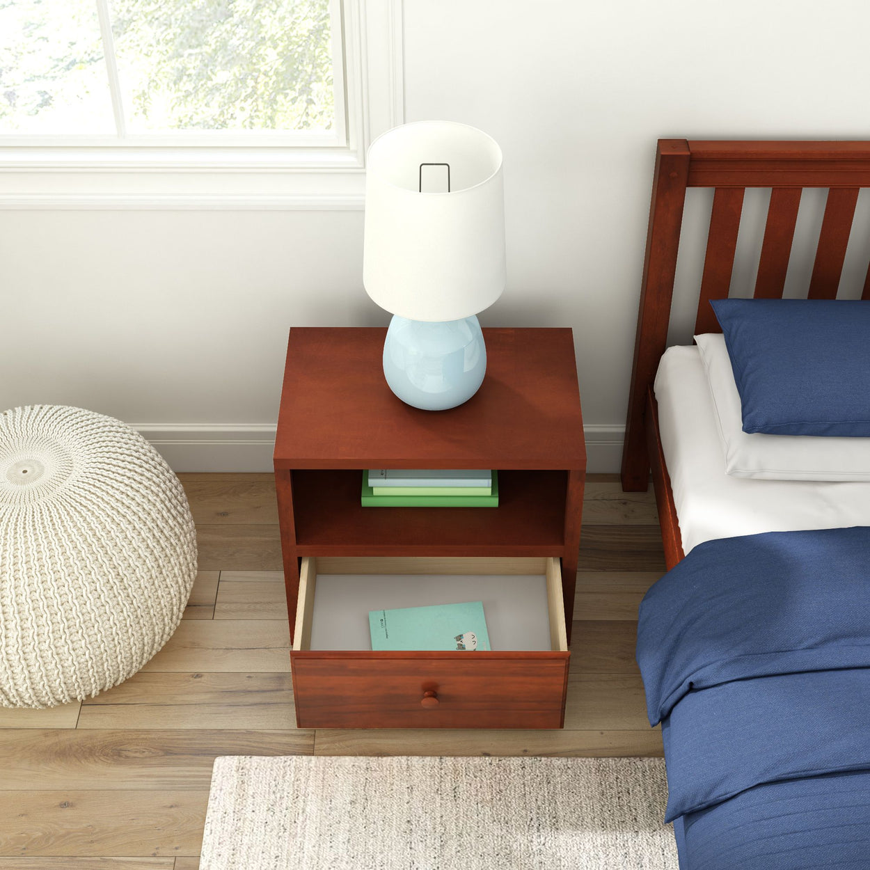 Wooden nightstand with open drawer and blue lamp beside bed with dark blue bedding in modern bedroom.