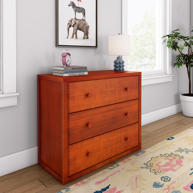Red wooden three-drawer dresser in a bright bedroom with table lamp, stacked books and pink alarm clock, framed animal print, potted plant and colorful area rug