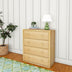 Modern wooden dresser with green table lamp and houseplant in stylish bedroom corner.