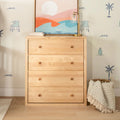 Light wood dresser with coastal abstract print, brass table lamp, beach-themed wall decals and woven basket with fringed throw blanket