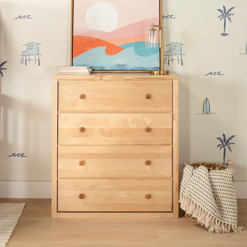 Light wood dresser with coastal abstract print, brass table lamp, beach-themed wall decals and woven basket with fringed throw blanket