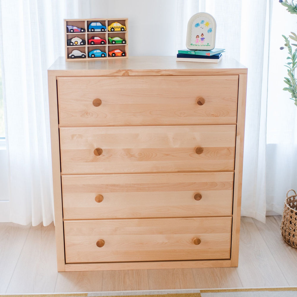 Light wood 4-drawer dresser in a bright nursery — minimalist children's room storage with wooden toy car organizer and framed kid's drawing on top