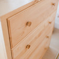 Close-up of light pine dresser drawers with round wooden knobs, natural wood grain and minimalist Scandinavian bedroom furniture