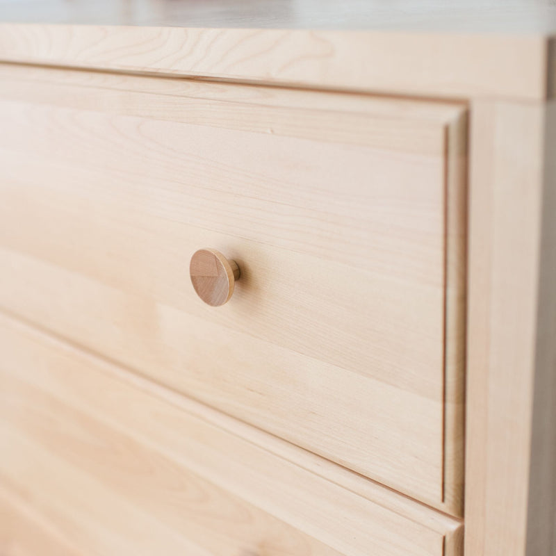 Close-up of light maple wood dresser drawer with round wooden knob and recessed handle, minimalist modern bedroom furniture