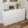 White six-drawer dresser in a minimalist bedroom styled with a vintage radio, brass table lamp, potted succulent, candle and books on top, hardwood floor and neutral wall art.
