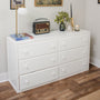 White six-drawer dresser in a minimalist bedroom styled with a vintage radio, brass table lamp, potted succulent, candle and books on top, hardwood floor and neutral wall art.