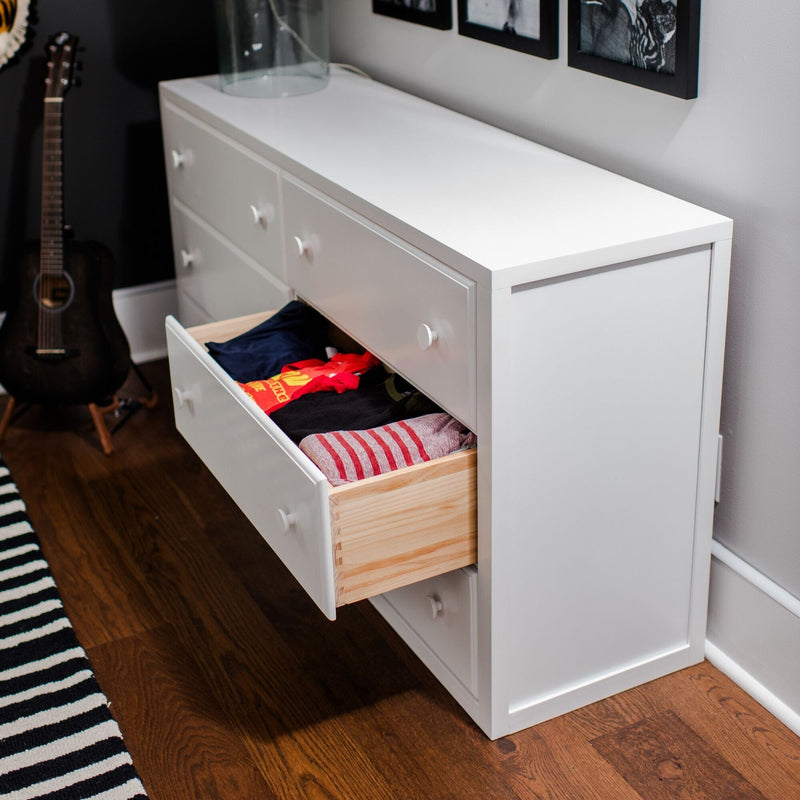 White dresser storage with open drawer showing neatly folded clothes in a modern bedroom with hardwood floor, acoustic guitar and striped rug