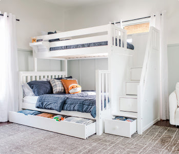 White wooden bunk bed with trundle drawer and built-in storage stairs, navy bedding and plush toy in bright modern kids' bedroom