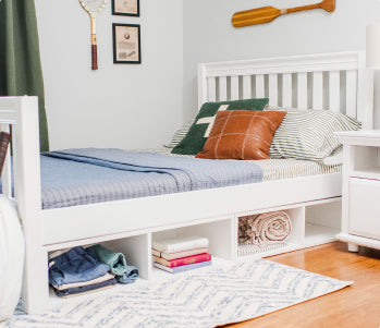 Cozy modern bedroom with white storage platform bed featuring under-bed cubbies, blue quilt and striped pillows, leather-look accent pillow, wooden oar wall decor and light hardwood floor