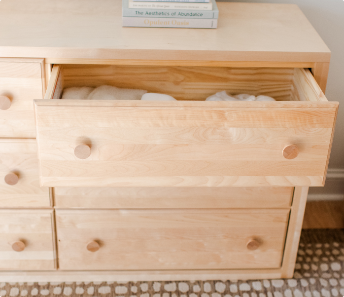 Light wood dresser with an open drawer filled with folded white towels, coastal bedroom decor featuring a decorative knot sculpture and ocean art print