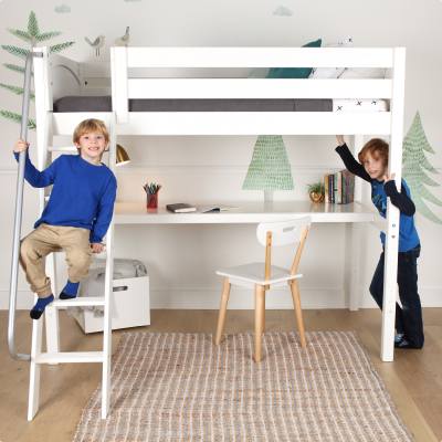 A white wooden loft bed with an integrated desk and chair, shown in a child's bedroom with two kids interacting with the bed frame.