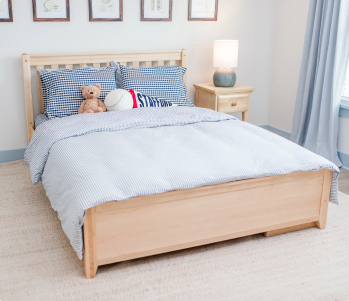 A white wooden toddler bed with a safety guard rail, styled in a child's bedroom with a woman and two young girls sitting on the bed.