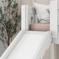 Modern white toddler bed with slide, blush pink mattress and white textured pillow against botanical wallpaper in a neutral nursery