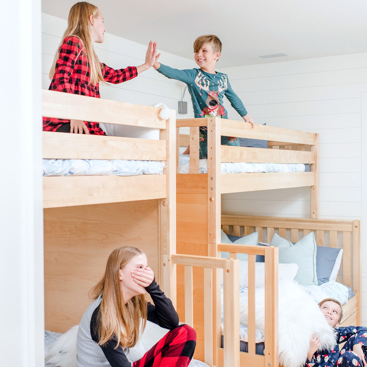 Children having fun in a cozy bedroom with wooden bunk beds, wearing colorful pajamas.