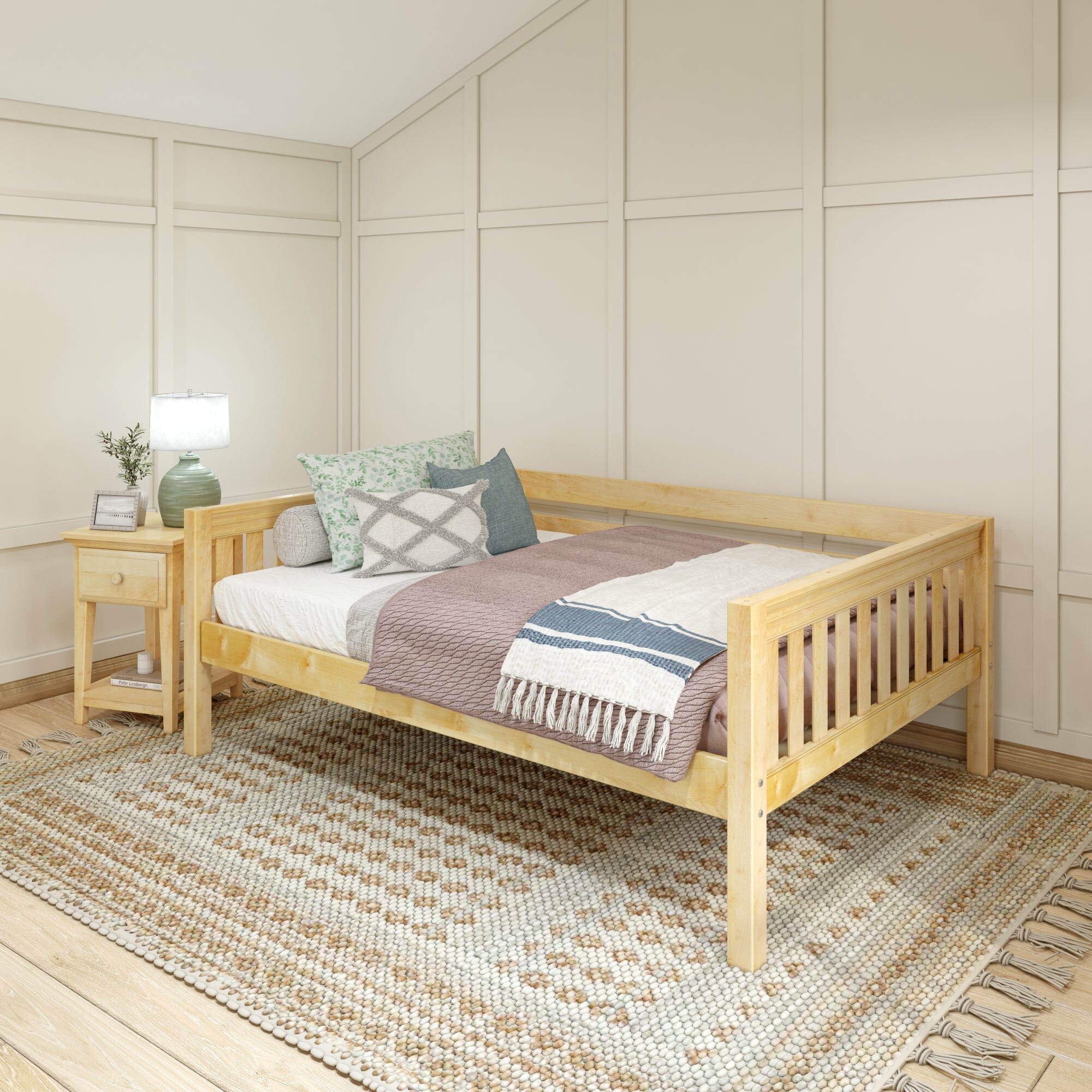 Wooden daybed with cozy pillows and blankets next to a bedside table and lamp in a bright, stylish room.