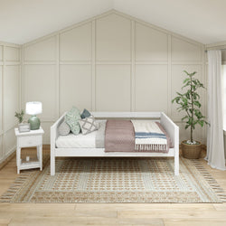 Cozy neutral farmhouse bedroom with white daybed, textured mauve and blue throws, patterned woven area rug, white nightstand with lamp, and potted plant against board-and-batten wall