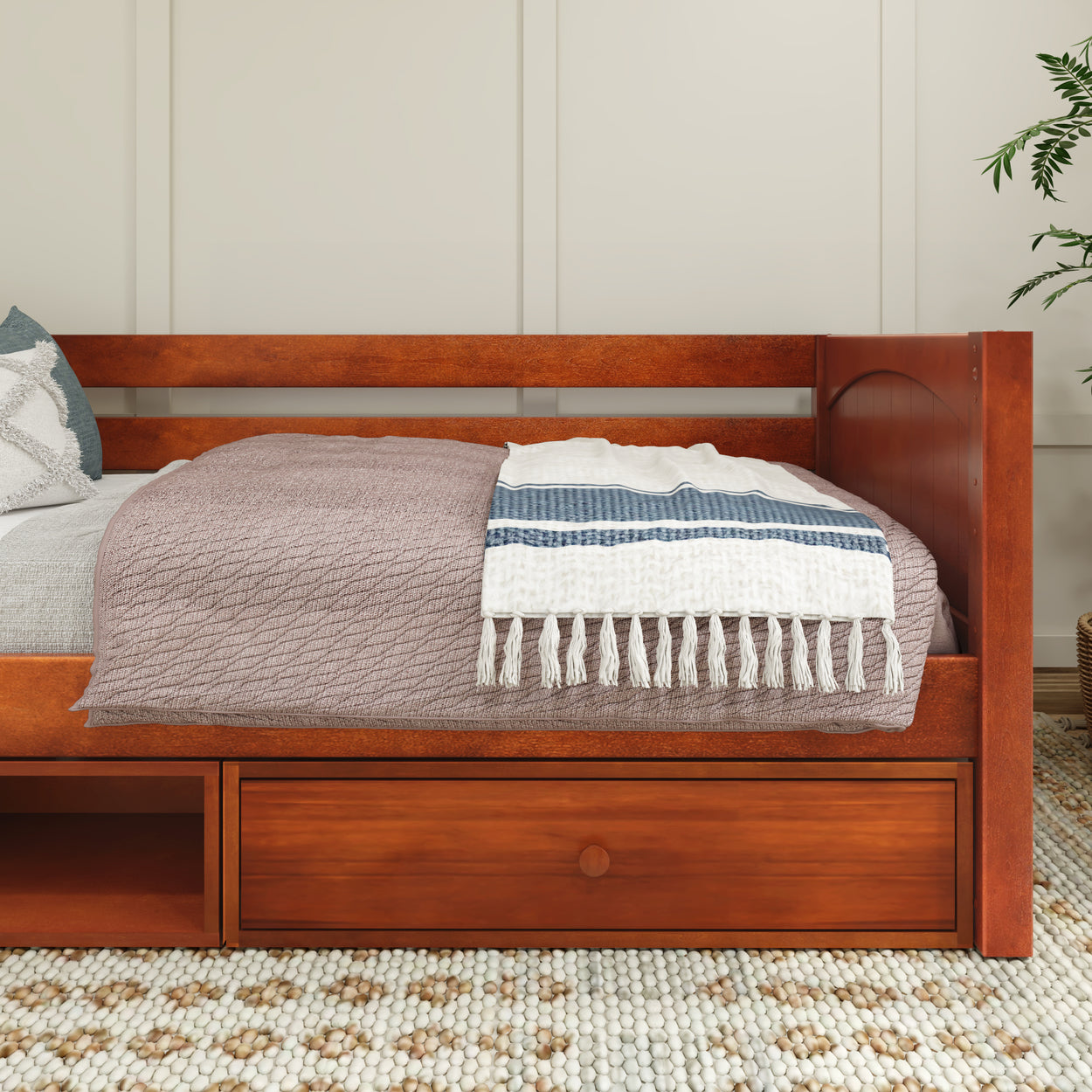 Wooden daybed with storage drawers, covered in cozy bedding and a decorative patterned blanket in a modern bedroom setting.