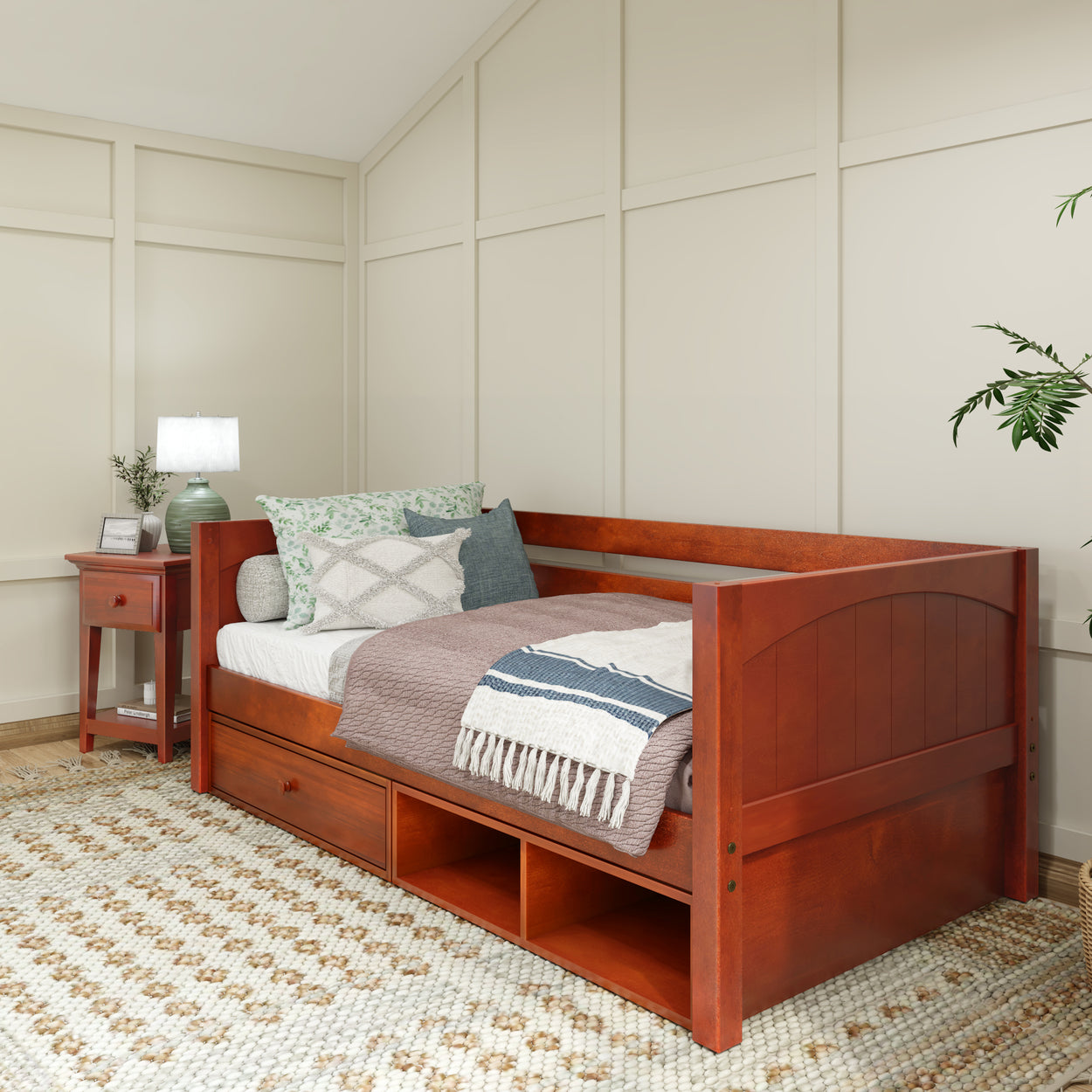 Wooden daybed with storage drawers in cozy bedroom setting with side table and decorative pillows.