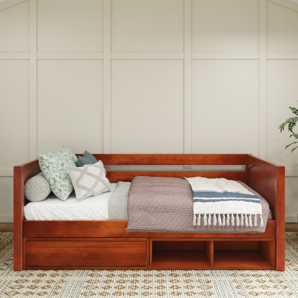 Wooden daybed with storage drawers, decorated with assorted pillows and blankets in cozy bedroom setting.