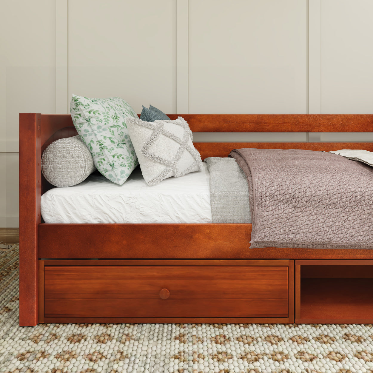 Wooden daybed with storage drawers, decorated with patterned pillows and a textured blanket in a cozy bedroom setting.