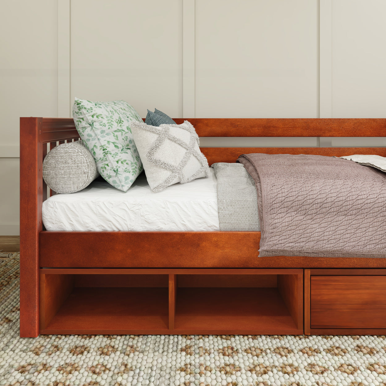 Wooden daybed with decorative pillows and cozy blanket on a patterned rug in a modern bedroom.