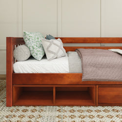Wooden daybed with decorative pillows and cozy blanket on a patterned rug in a modern bedroom.