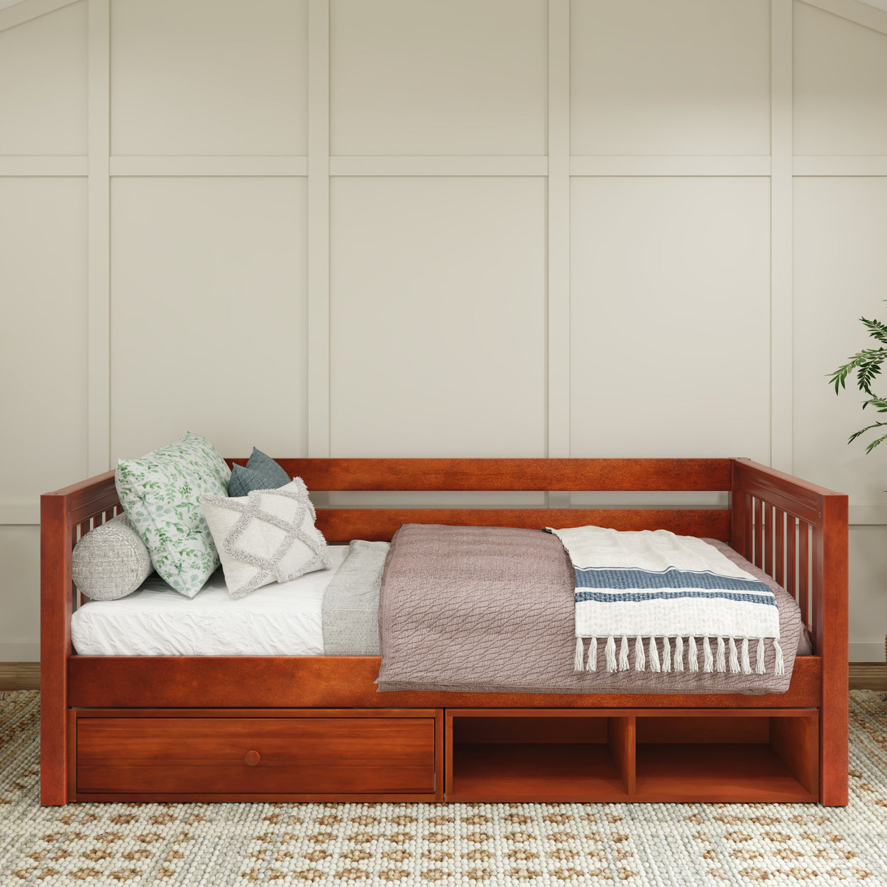 Wooden daybed with storage drawers, adorned with decorative pillows and blankets in a cozy, modern bedroom setting.