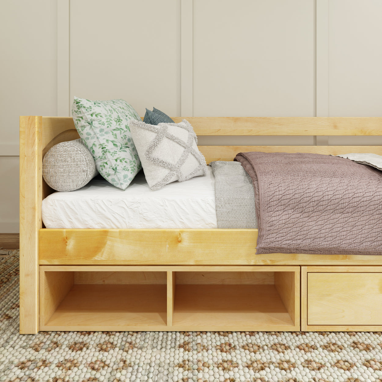 Cozy modern daybed with wooden frame, decorative pillows, and knitted throw blanket on textured carpet in light-filled bedroom.