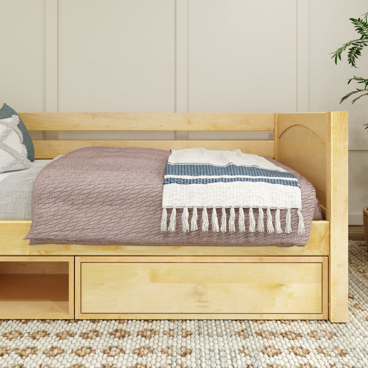 Natural wood daybed with storage drawers, draped with a cozy blanket and throw pillow in a modern bedroom setting.