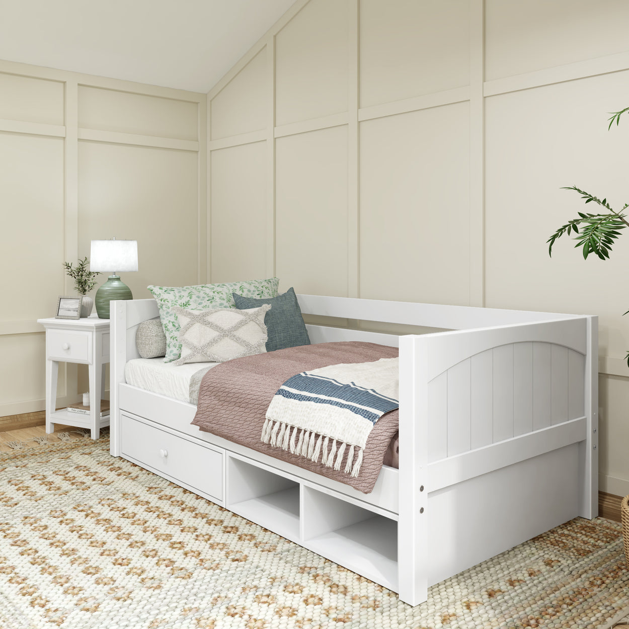 White daybed in cozy bedroom with cushions, bedside table, and patterned rug.
